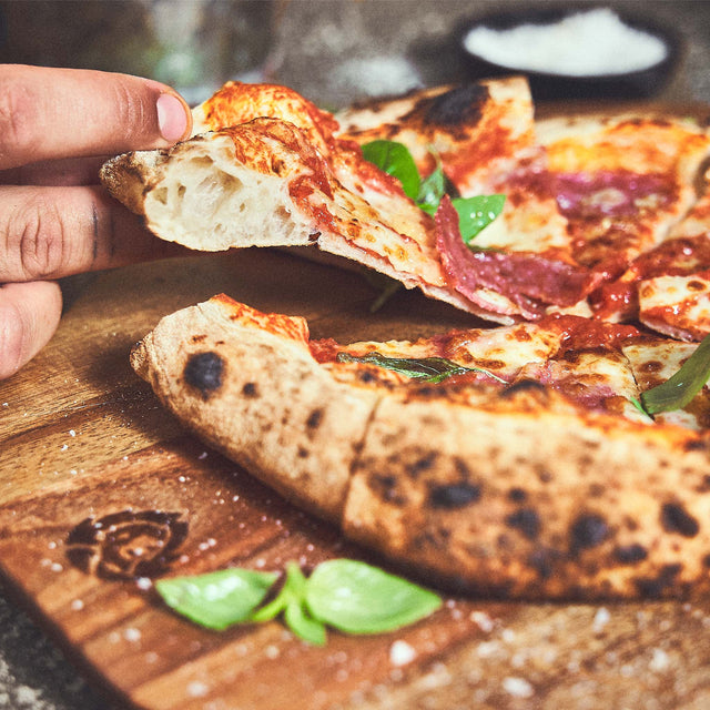 946411, 946593 Afgewerkte pizza wordt van de acaciahouten pizzaplaat gehaald